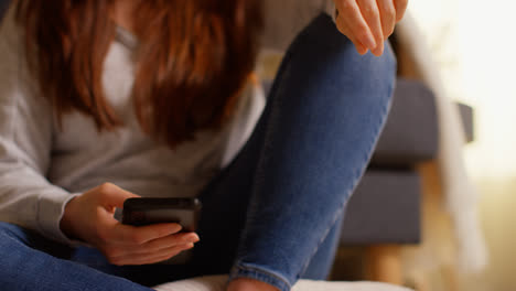 Primer-Plano-De-La-Mano-De-Una-Mujer-Sentada-En-Un-Sofá-En-Casa-Usando-Un-Teléfono-Móvil-Para-Revisar-Los-Mensajes-De-Las-Redes-Sociales-Y-Desplazarse-En-Línea-2